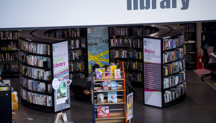 Circular bookshelves under the mezzanine which has the word 'Library' written across it.