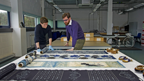 Two curators at work in the Research Room at GMRC viewing textile objects laid flat on a table