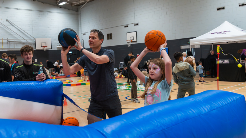 An adult and child are holding basketballs at head height which they are about to throw.
